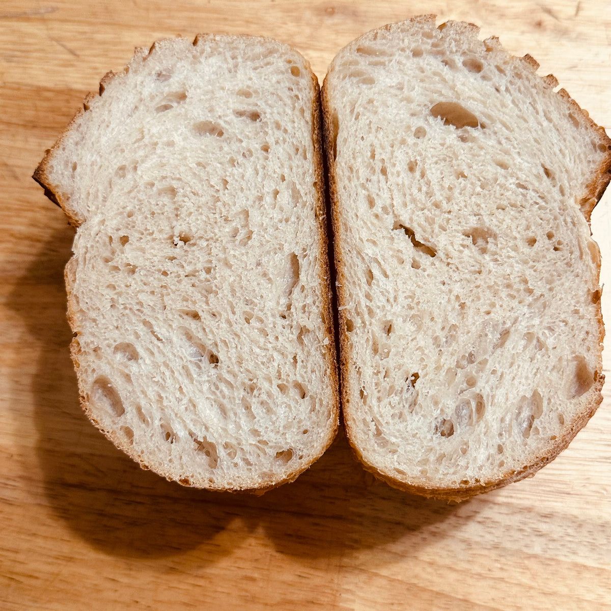 Two thick slices of rustic whole wheat bread with a golden-brown crust, cut lengthwise, displayed on a wooden cutting board.